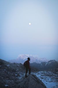 Rear view of person standing on snowcapped mountain against sky