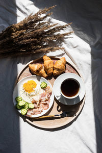 Breakfast in bed coffee cup, fried egg, bacon and croissants on wooden tray. 