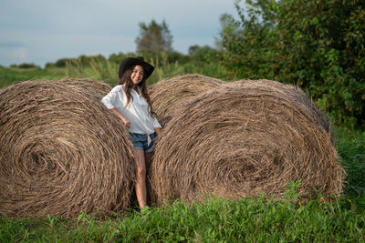 Young woman standing on field near the haystack 
