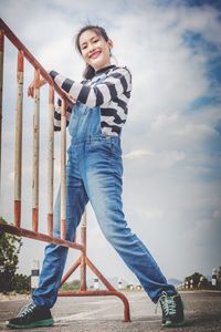  portrait of smiling young woman standing against sky and caught a fence