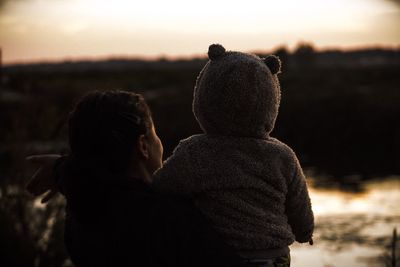 Silhouette mother carrying son while standing against sky during sunset