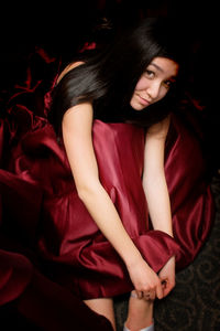 Portrait of woman wearing red dress sitting in darkroom