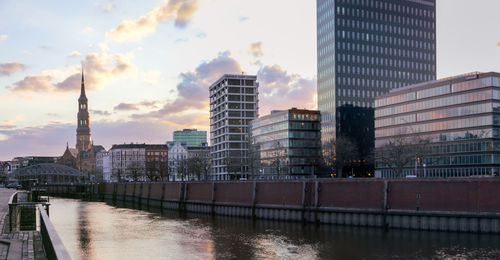 Buildings by river against sky during sunset in city