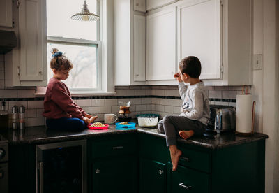 Brother and sister sitting in kitchen together eating waffles