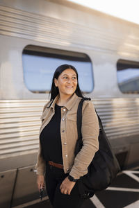 Smiling mid adult woman standing at train station looking away