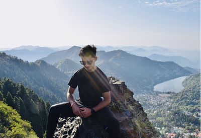 Woman sitting on mountain against sky