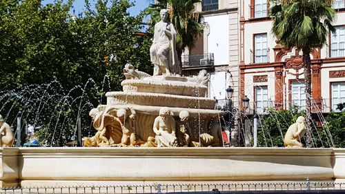 Statue by fountain against trees and building