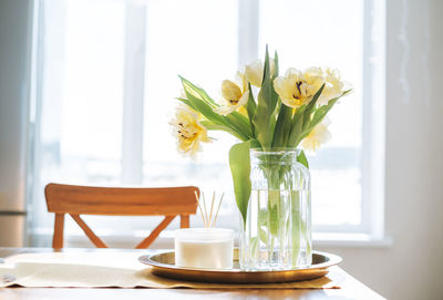 Beautiful bouquet of yellow tulips in vase on dinner table in white kitchen light interior at home