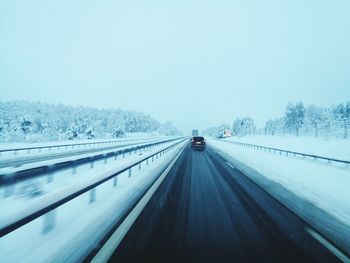 Cars on road against clear sky during winter