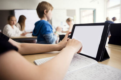 Cropped image of boy using digital tablet in classroom