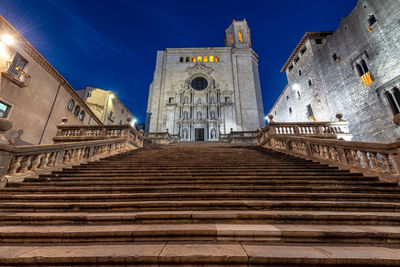 Low angle view of steps leading towards church amidst buildings against blue sky