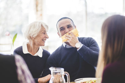 Cheerful senior woman with son wiping mouth with tissue paper while having lunch in nursing home