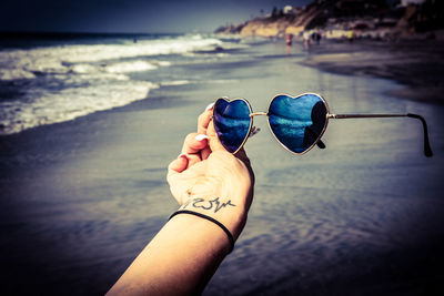 Close-up of hand holding sunglasses against sea