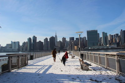 People on snow covered bridge against cityscape