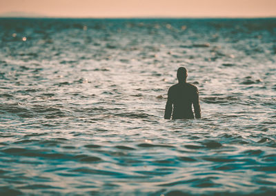 Rear view of silhouette man swimming in sea during sunset