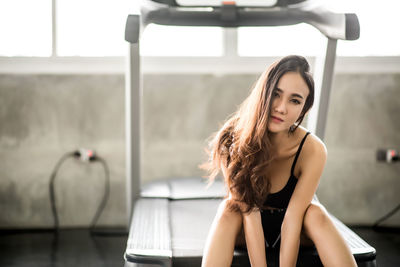 Portrait of young woman sitting on treadmill while exercising in gym