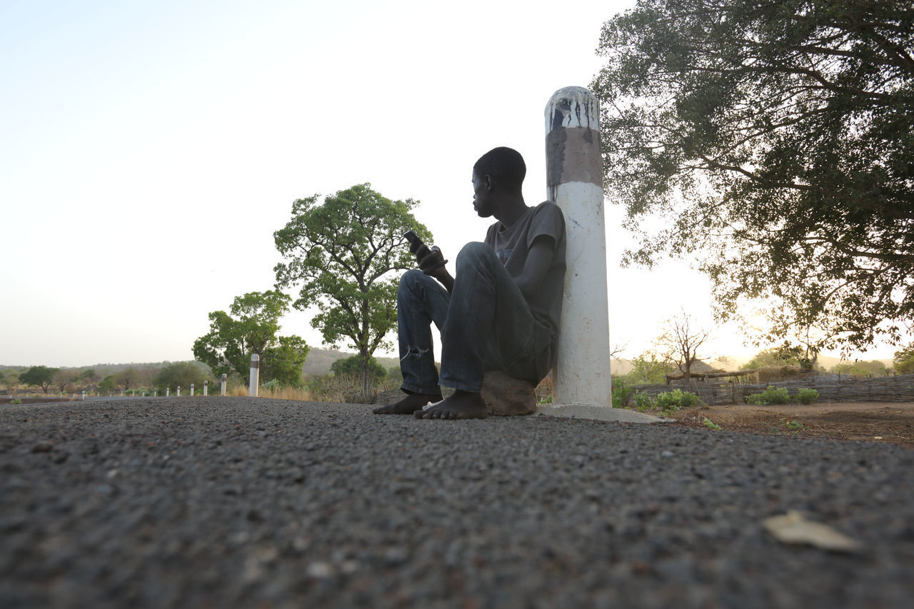 STATUE OF MAN SITTING ON ROAD AGAINST CLEAR SKY