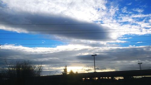 Low angle view of power lines against cloudy sky