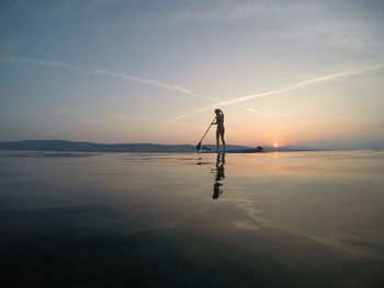 Silhouette woman paddleboarding in sea against sky during sunset