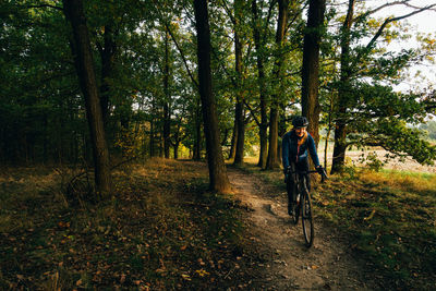 Smiling woman riding bicycle amidst trees in forest