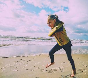 Girl jogging on beach against sky during sunny day