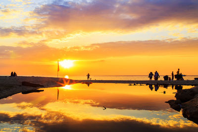 Silhouette people on sea against sky during sunset