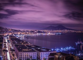 High angle view of illuminated city by river against sky at dusk