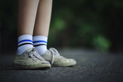 Low section of person wearing canvas shoes while standing on walkway