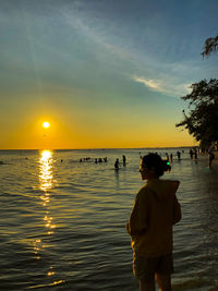 Rear view of woman standing at beach against sky during sunset