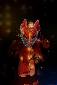 Anonymous woman in creative fox mask with neon ornaments working during party in nightclub