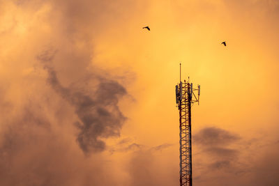 Low angle view of communications tower against orange sky