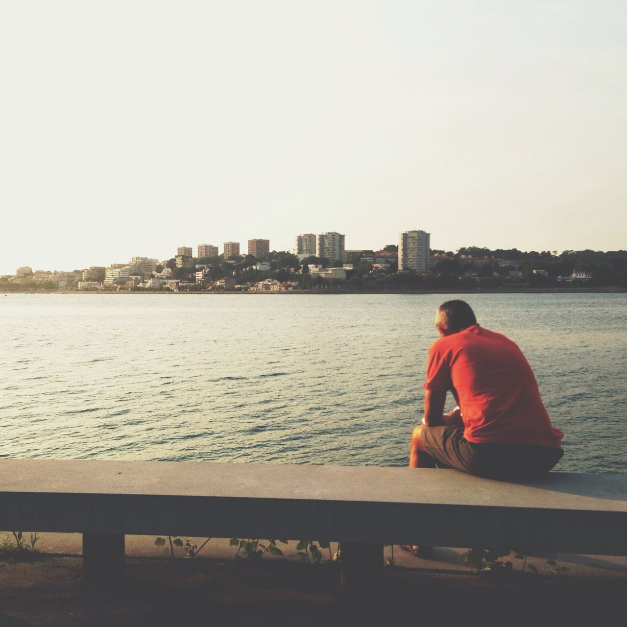 water, clear sky, rear view, copy space, built structure, building exterior, sitting, architecture, lifestyles, river, city, leisure activity, men, looking at view, standing, relaxation, casual clothing, railing