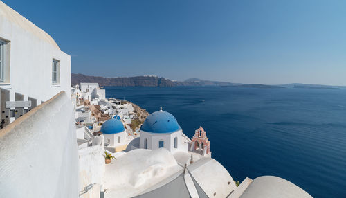 Buildings by sea against clear blue sky