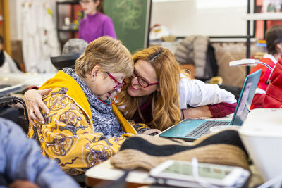 Smiling female caregiver talking with disabled woman by laptop at rehabilitation center