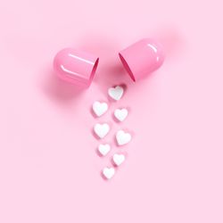 High angle view of heart shape pills by capsule against pink background