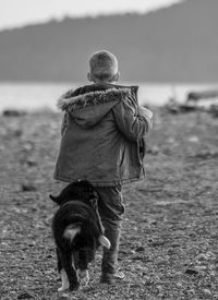 Rear view of boy playing with dog at beach