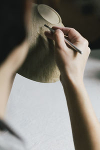 Cropped image of craftswoman painting bowl in workshop