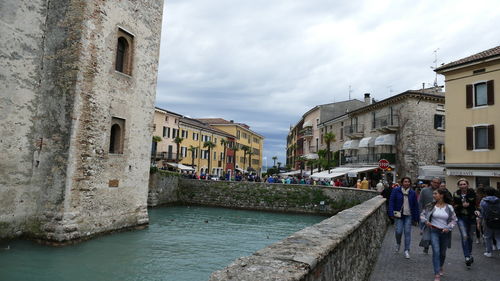 People on canal amidst buildings in city against sky