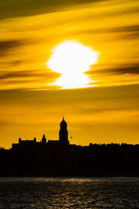 Silhouette built structure by sea against orange sky