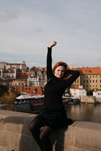 Portrait of young woman standing in city against sky