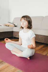 The girl sits in the lotus position and meditates at home in the living room. yoga poses for kids