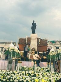 Statue by flowers against sky