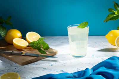 Glass with lemonade and lemons on wooden table, cold refreshing drink with ice on light background.
