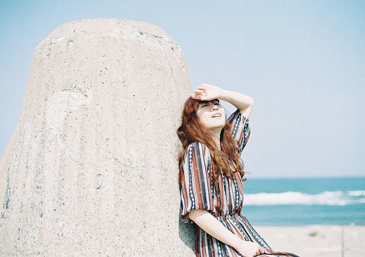 SMILING YOUNG WOMAN STANDING AGAINST SEA