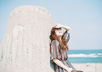 Smiling young woman standing against sea against sky