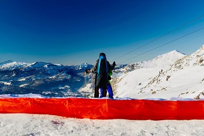 Woman standing on snowcapped mountain against blue sky