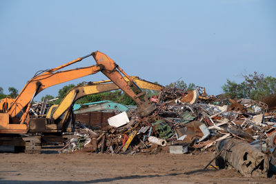 Excavator magnet lifting steel scraps from recycling materials pile at scrap yard in recycling