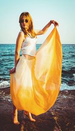 Portrait of young woman standing by sea against sky