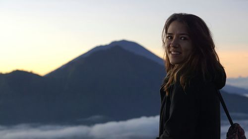 Portrait of smiling young woman standing against sky during sunset