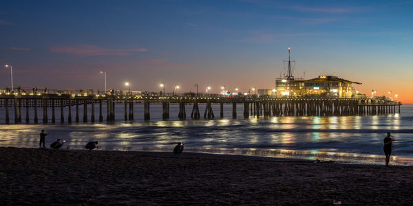 Illuminated buildings by sea against sky at night